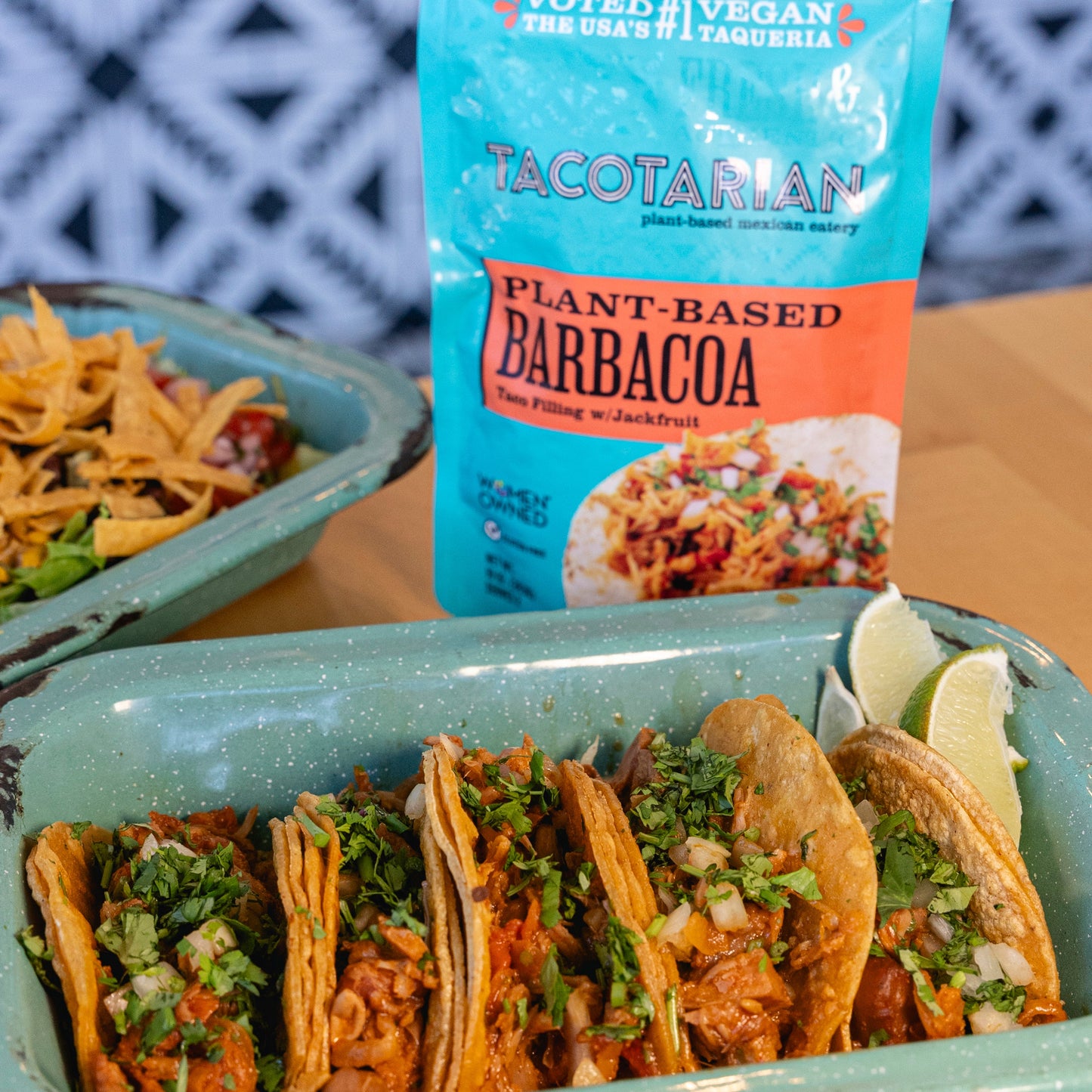 Tacos in a green tray with a package of Tacotarian Barbacoa on a wooden surface.